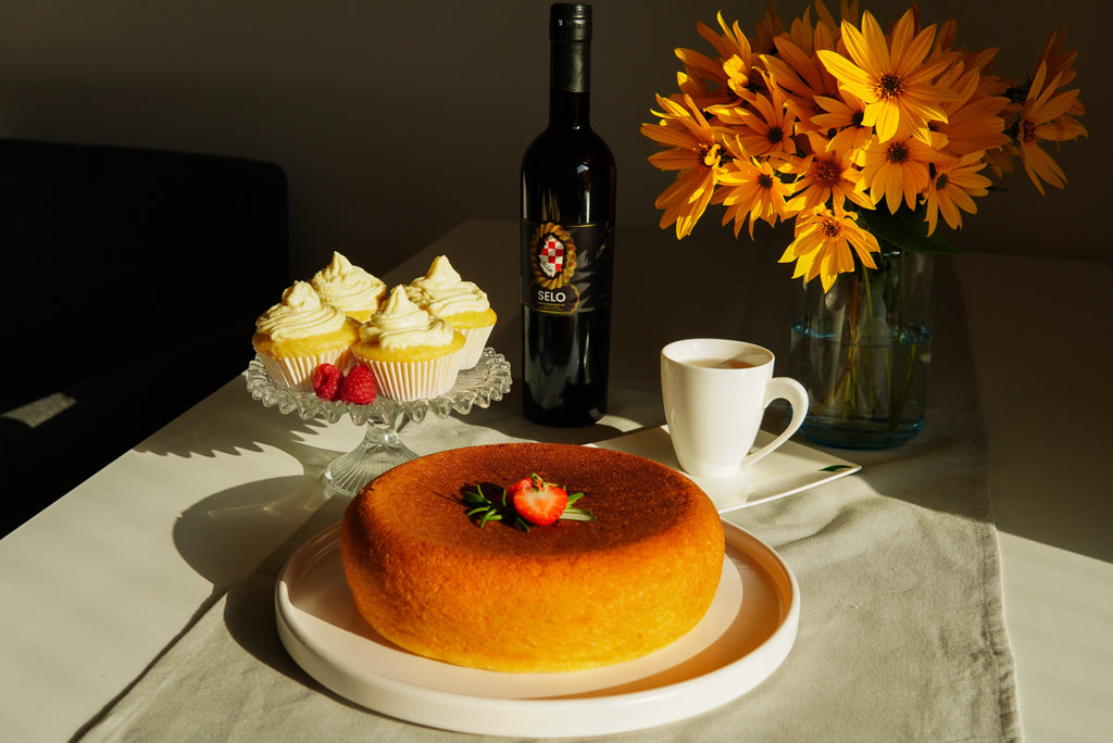 Image of a moist, golden cake baked with Selo Croatian extra virgin olive oil, displayed on a rustic wooden table with a bottle of Selo olive oil in the background.