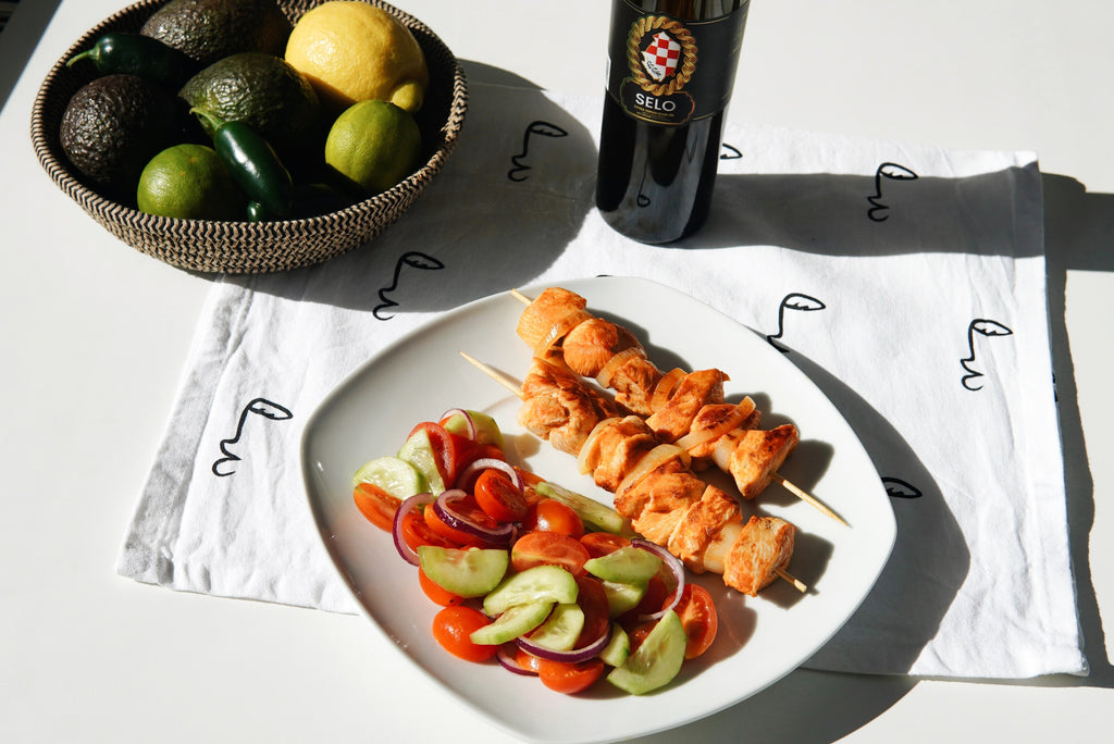 Grilled Meat Skewers (Ražnjići) on a plate with a colorful Cucumber and Tomato Salad, garnished with fresh parsley.