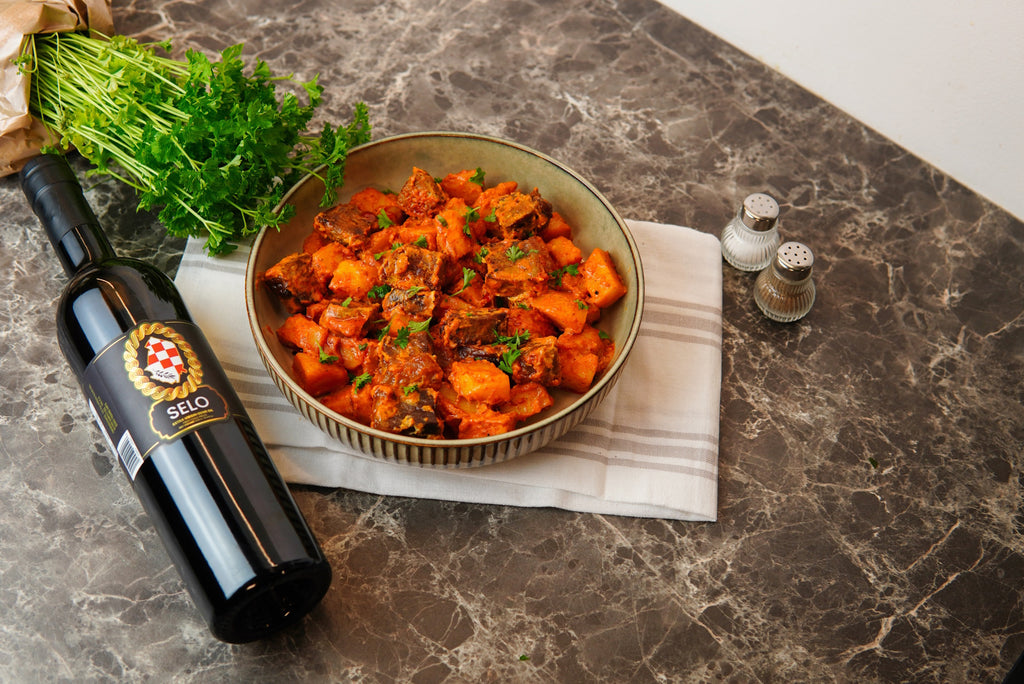 A mouthwatering Chicken Goulash simmered in a rich sauce, enhanced by a touch of Croatian olive oil, served in a rustic bowl with crusty bread for dipping.